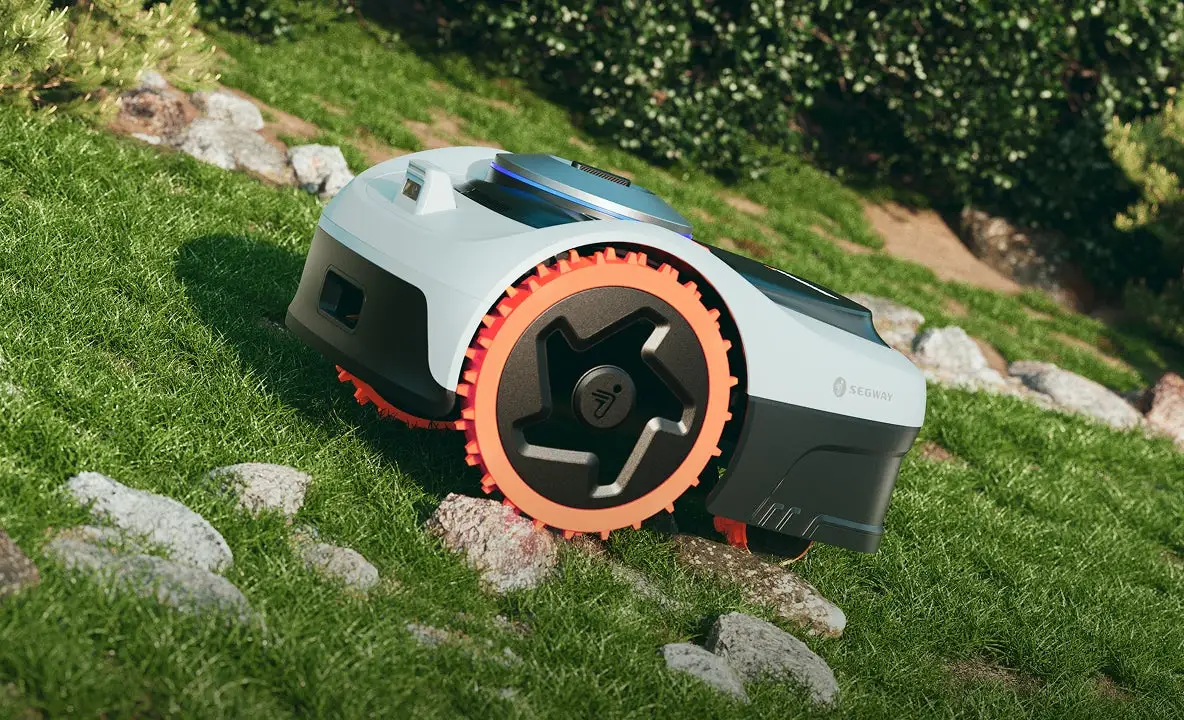 Segway Navimow i2 AWD robot mower climbing a grass bank between rocks on its orange 9.8 inch off-road drive wheels